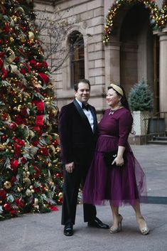 a man and woman standing next to a christmas tree in front of a large building