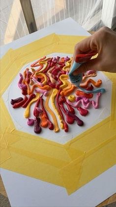 a person is painting letters on a white surface with yellow and red paint, while the other hand holds a blue marker