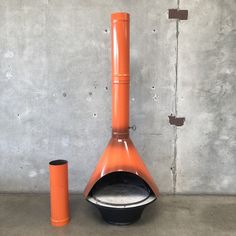 an orange and black stove sitting on top of a cement floor next to a cup