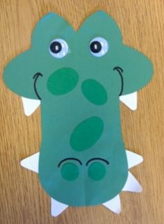 a paper cut out of a green crocodile with big eyes and long tail sitting on top of a wooden table