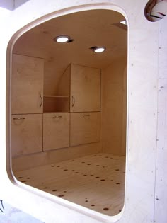 an empty room with wooden cabinets and lights on the ceiling is seen through a circular window