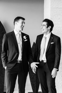 two men standing next to each other wearing suits and smiling at each other's side