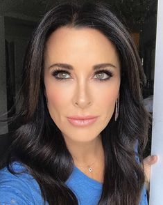 a woman with long dark hair and blue shirt looking at the camera while wearing earrings