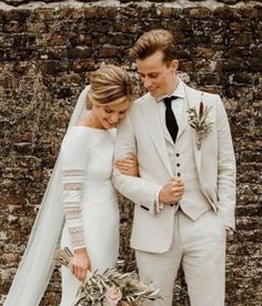 a bride and groom standing next to each other in front of a brick wall with flowers