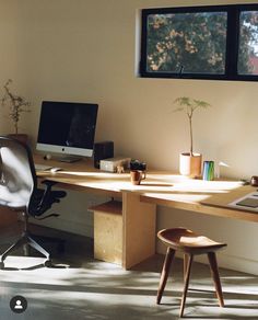 a desk with a computer, chair and potted plant in the window sill