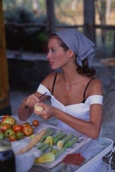 a woman sitting at a table with an apple in her hand and vegetables on the table