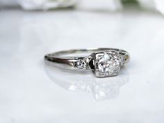 an engagement ring with three stones on it sitting on a white surface next to flowers