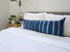 a bed with white linens and blue striped pillow on it's headboard