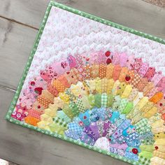 a multicolored quilt on a wooden surface with a colorful fan design in the center