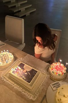 a woman sitting at a table in front of two cakes with candles on top of them