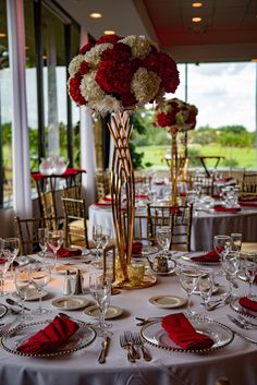 the table is set with silverware, red napkins and flowers in tall vases