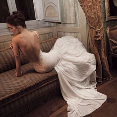 a woman sitting on top of a couch in front of a window wearing a dress