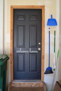 a black front door with welcome home written on it and brooms next to it