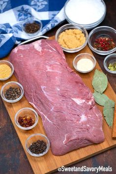 a large piece of meat sitting on top of a wooden cutting board next to bowls of spices and seasonings