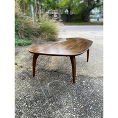 a small wooden table sitting on top of a cement ground next to some grass and trees