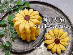 two small yellow flowers sitting on top of a metal plate next to green leaves with the words sunflower pastry written in chinese