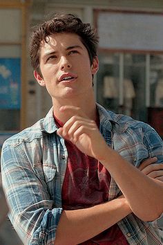 a young man standing in front of a building with his arms crossed and looking up