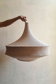 a person is holding a woven basket in their hand and it's hanging from the ceiling