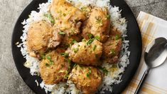 a black plate topped with chicken and rice next to a fork on top of a table