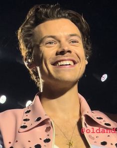 a man in a pink jacket smiles at the camera while standing on stage with lights behind him