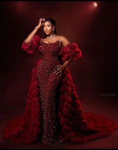 a woman in a red gown posing for the camera with her hands on her head