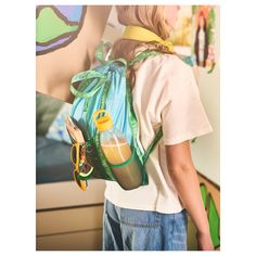 a girl wearing a backpack with an orange juice in the bottom pocket and a green strap around her neck