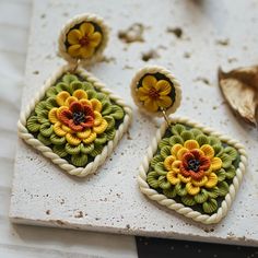 the earrings are decorated with colorful flowers and braided in thread, sitting on a marble slab