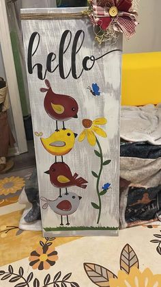 a wooden sign that says hello with birds and flowers on the front, sitting on a table