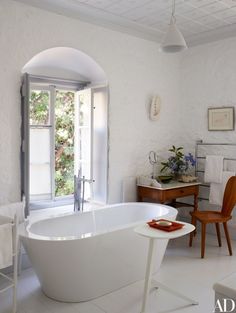 a white bath tub sitting in a bathroom next to a wooden chair and table with flowers on it