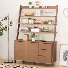 a wooden shelf with plants and pictures on it next to a clock, potted plant and other items