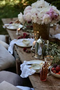 the table is set with plates and bowls of fruit, flowers, and silverware