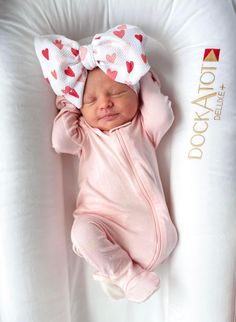 a newborn baby wearing a pink outfit and a bow laying on top of a pillow