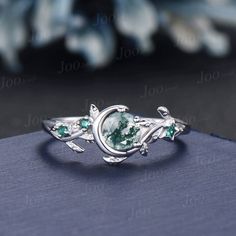 a ring with green stones and leaves on it, sitting on top of a blue book