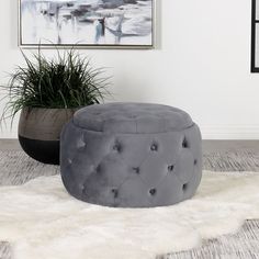 a grey ottoman sitting on top of a white rug next to a potted plant