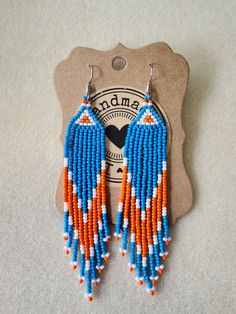 a pair of beaded earrings with orange and blue beads hanging from it's earwires