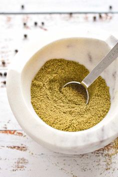 a white bowl filled with green powder and a measuring spoon