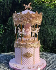 a pink and gold carousel cake sitting on top of a table