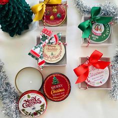 four christmas gift boxes with ribbons and tags on them, sitting next to some tinsel