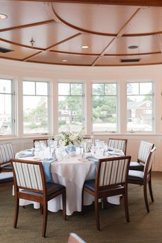 a dining room set up with white table cloths and blue striped chairs in front of large windows