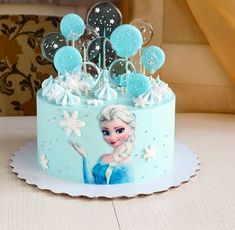 a frozen princess cake with blue frosting and balloons on top, sitting on a table