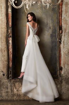 a woman in a white wedding dress standing against a wall with chandelier hanging from it