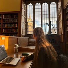 a woman sitting at a table with a laptop computer in front of her and bookshelves behind her