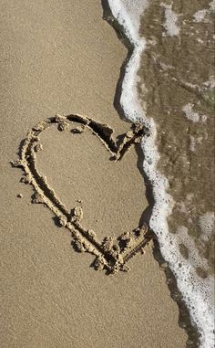 a heart drawn in the sand at the beach with waves coming in and out behind it