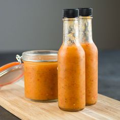 two bottles filled with sauce sitting on top of a wooden tray