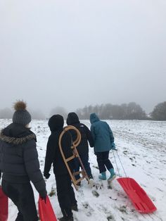 four people walking in the snow with sleds