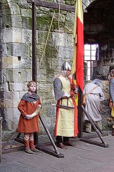 two men in medieval costumes standing next to each other with flags and poles behind them