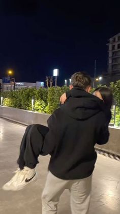 two people are hugging on the roof of a building at night with lights in the background