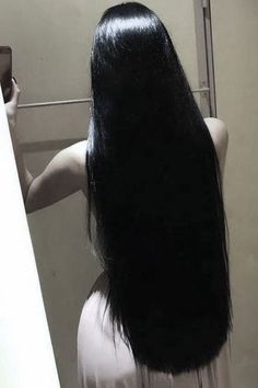 a woman with long black hair standing in front of a mirror