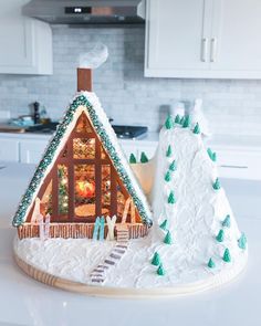 a cake shaped like a cabin with trees and snow on the roof is sitting on a kitchen counter