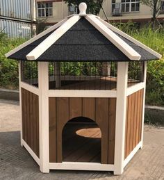 a small wooden dog house with a black roof and white trim on the top, in front of some buildings